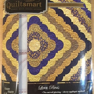 May include: Quiltsmart Love Ring printed interfacing pattern for quilting. The pattern features a purple and gold design with a circular motif. The text on the packaging reads "Easy! Fast! Smart!" and "No curved piecing - clever appliqué method! Square blocks sew up easily! You'll love the beautiful results!"