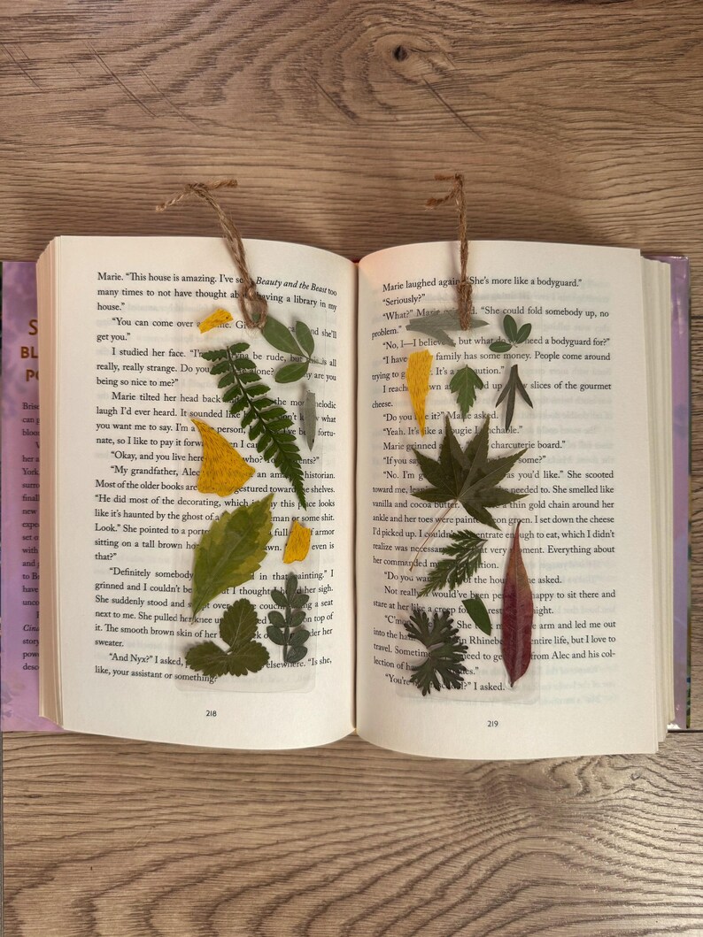 May include: Two open books with pressed flowers and leaves as bookmarks. The text on the left page reads "Beauty and the Beast" and the text on the right page reads "She's more like a bodyguard".