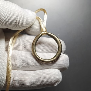 May include: A gold-coloured ring pendant with a simple circular design, hanging from a cream-coloured cord.