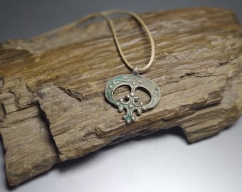 May include: A silver pendant necklace with a detailed design featuring a circle with a cross inside. The pendant is hanging on a brown leather cord and is resting on a piece of wood.