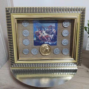 Puede incluir: Una imagen enmarcada con un marco dorado y plateado. La imagen es una pintura de un grupo de personas en un entorno clásico. Hay 12 monedas de plata alrededor de la pintura.