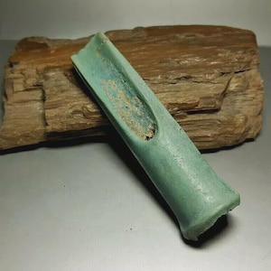 May include: A weathered, turquoise-colored, elongated object with a hollowed-out center. The object has a slightly curved shape and appears to be made of a solid material. It rests on a piece of brown, textured wood.