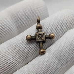 Könnte beinhalten: Ein kleiner, antiker Bronze-Kreuzanhänger mit einem quadratischen Zentrum und vier runden Akzenten. Das Kreuz ist aufwendig verziert und hat eine Patina.