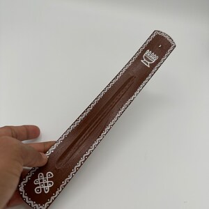 Op de afbeelding: Bruine houten wierookbrander met witte geverfde ontwerpen. De ontwerpen omvatten een gestileerde bloem en een knoop.