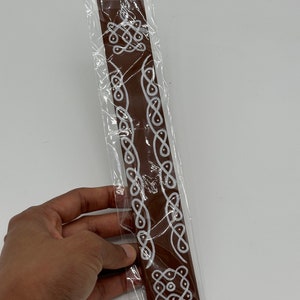 Op de afbeelding: Een bruine wierookstok met witte decoratieve ontwerpen. De stok is verpakt in doorzichtig plastic.