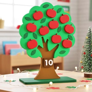 Może przedstawiać: Drewniane drzewo jabłoni z czerwonymi jabłkami i numerem 10 na pniu. Mała choinka i łańcuchy świetlne znajdują się na stole. Drzewo jest zielone z czerwonymi jabłkami.
