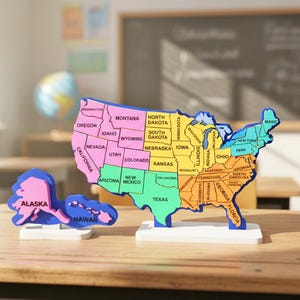 Puede incluir: Rompecabezas de madera colorido de los Estados Unidos, con cada estado etiquetado y pintado de un color diferente. El estado de Alaska está separado. El rompecabezas está sobre un escritorio de madera en un aula.