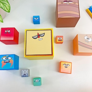 May include: A collection of colorful, cube-shaped toys with cartoon faces. The cubes are various colors, including red, blue, orange, and yellow. Each cube features a unique facial expression, creating a playful and engaging design.