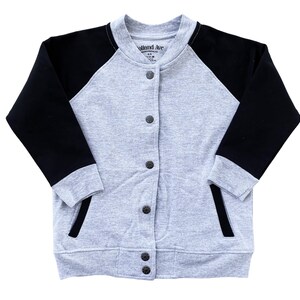 Op de afbeelding: Een grijs en zwart baseballjack met een knoopsluiting. De mouwen zijn zwart en de body is grijs. De jas heeft twee voorzakken en de tekst "Holland Ave" op het label.