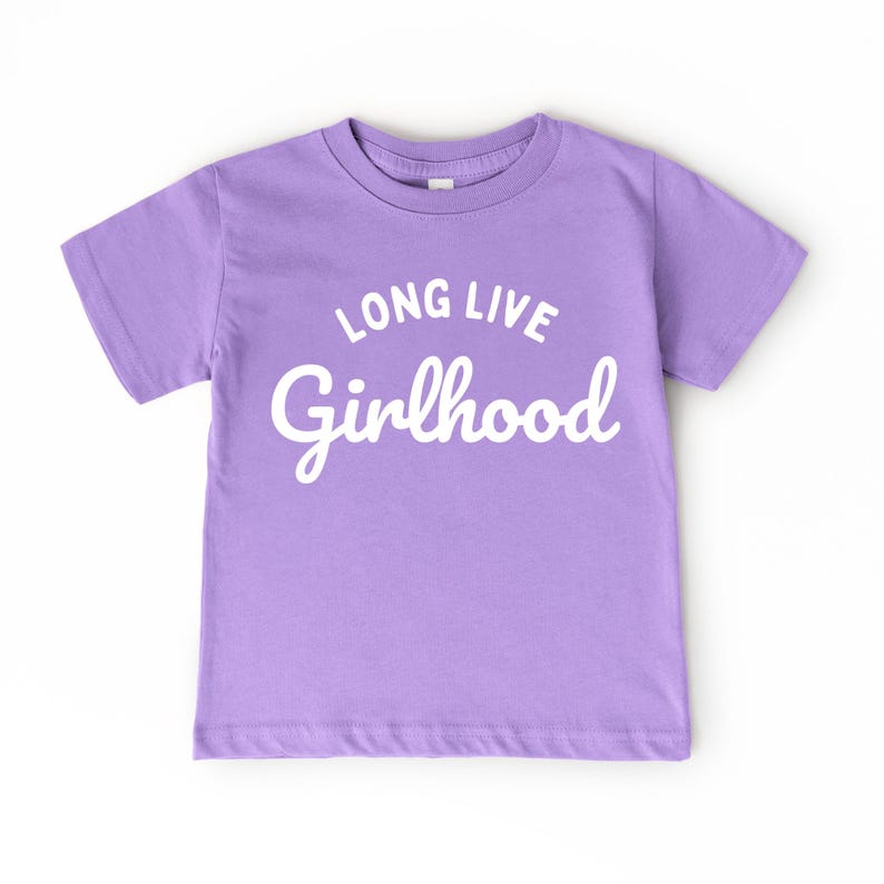 May include: A lilac-colored t-shirt with the words "LONG LIVE Girlhood" in white script. The shirt has short sleeves and a crew neck. The text is centered on the front of the shirt.
