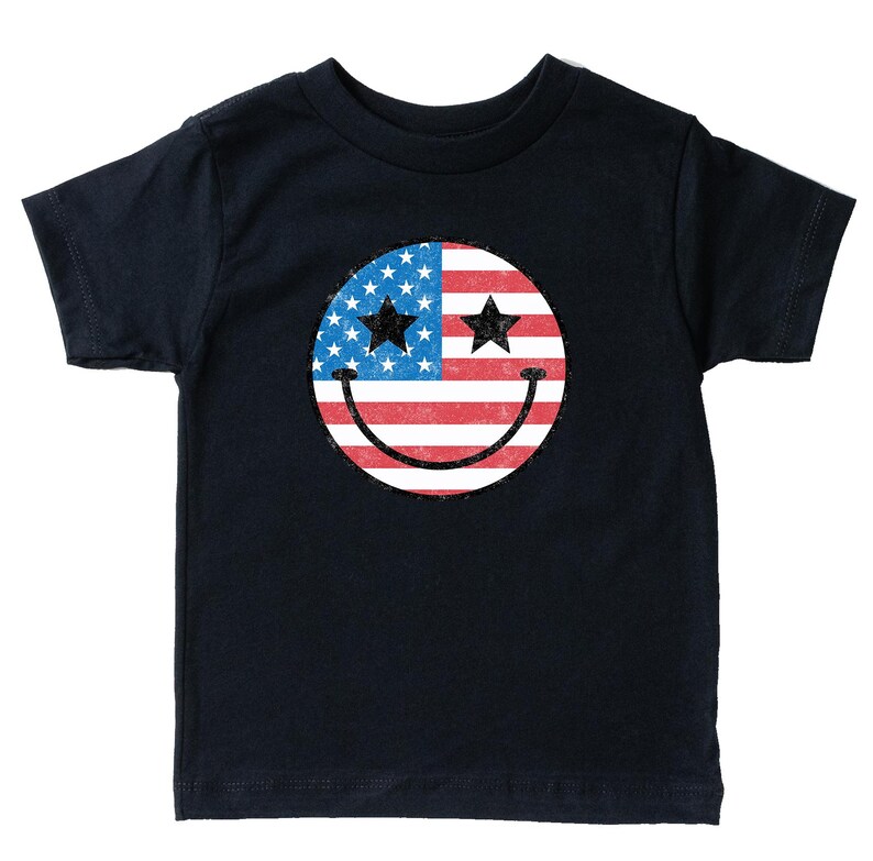 Op de afbeelding: Een marineblauw T-shirt met een versleten smiley-gezicht ontwerp. De smiley bevat de Amerikaanse vlag, met sterren en strepen, en twee zwarte sterrenogen. Het ontwerp is gecentreerd op de voorkant van het shirt.