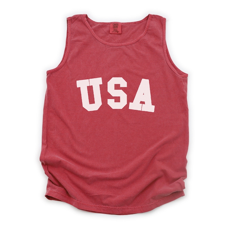Pu&ograve; includere: Canotta rossa senza maniche con la scritta "USA" stampata in bianco sul davanti.