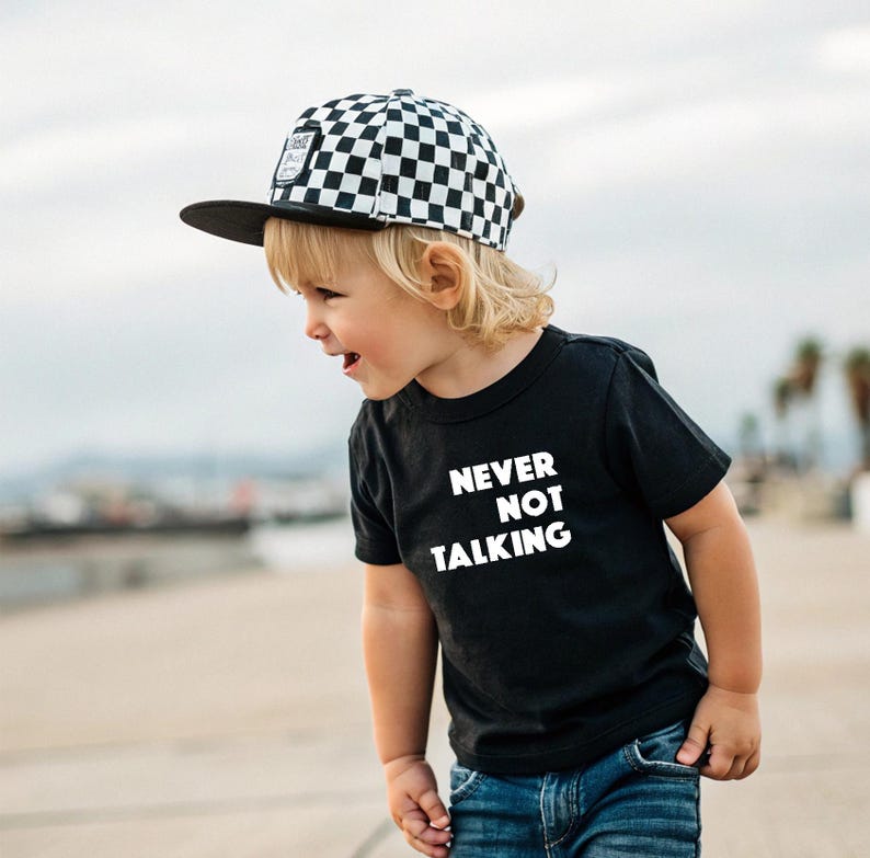 May include: A black short-sleeve t-shirt featuring the white text NEVER NOT TALKING printed on the front, paired with a black and white checkered baseball cap with a flat brim and a small rectangular patch on the front panel.