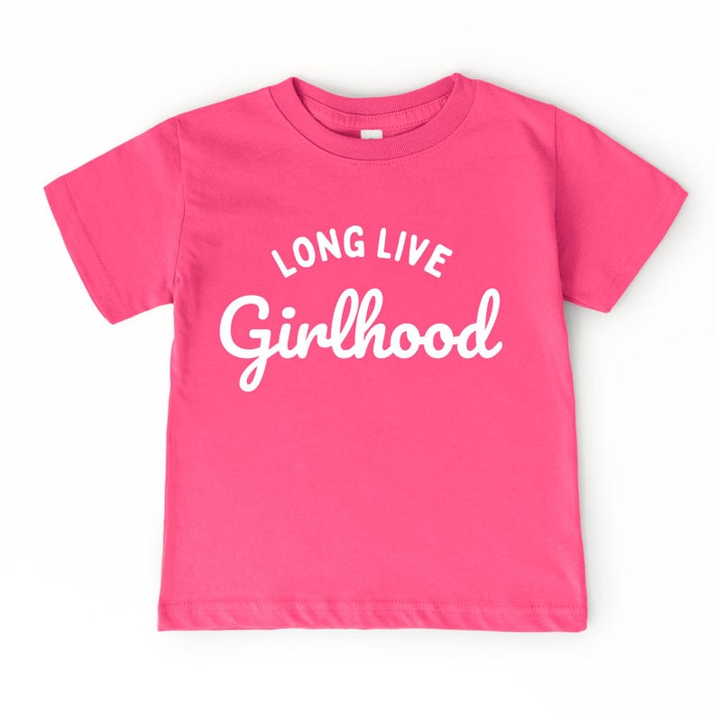 May include: A bright pink t-shirt with the words "LONG LIVE Girlhood" in white script. The shirt has short sleeves and a crew neck. The text is centered on the front of the shirt.