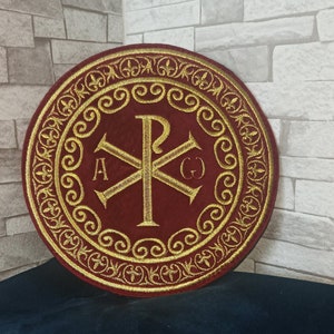May include: A red circular embroidered patch with a gold Greek cross and the letters 'A', 'P', 'O', and 'E' around the cross. The patch has a gold decorative border.