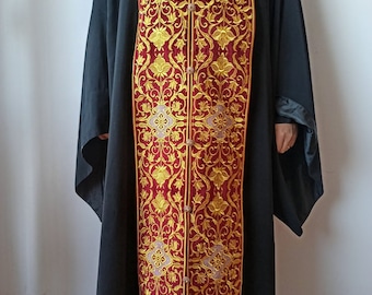 Pode incluir: Uma longa veste litúrgica de cor bordô com bordados dourados. A veste tem um padrão floral e é adornada com franjas douradas.