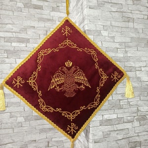 May include: A red velvet square cushion with gold embroidered trim and tassels. The center features a gold embroidered double-headed eagle with a crown and a cross. The text "A&Omicron;&Omega;" is embroidered in the corners.