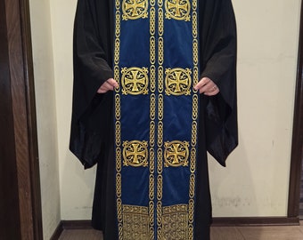 Pode incluir: Uma veste litúrgica azul com bordados dourados de cruzes e padrões intrincados. A veste tem um design longo e fluido e apresenta borlas na parte inferior.