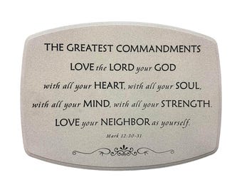 May include: A rectangular, light-colored plaque with rounded corners, featuring the text "THE GREATEST COMMANDMENTS" and a quote from Mark 12:30-31. The text is in black, with decorative flourishes at the bottom.