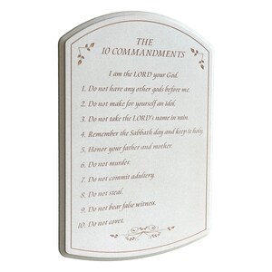 May include: A rectangular, off-white plaque with a decorative border and the text "THE 10 COMMANDMENTS" in a serif font. The text of the commandments is printed below in a smaller font. Floral accents are in the corners.