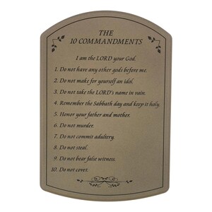 May include: A rectangular plaque with rounded top edges, featuring the text "THE 10 COMMANDMENTS." The text of the commandments is printed in black on a beige background, with decorative floral accents at the top and bottom.