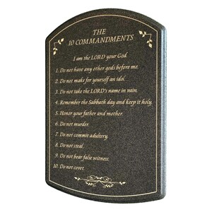 May include: A dark gray plaque with the text "THE 10 COMMANDMENTS" and the Ten Commandments listed below. The text is in gold, with decorative gold accents at the top and bottom. The plaque has a curved top.