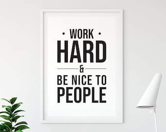 Puede incluir: Un póster enmarcado blanco con texto negro que dice "Trabaja duro y sé amable con la gente". El póster está colgado en una pared blanca con una silla de madera y una lámpara blanca en el fondo.