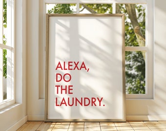 May include: A framed print with the text "ALEXA, DO THE LAUNDRY" in red letters. The framed art is leaning against a white wall next to a window with natural light. The frame is a light gold color.