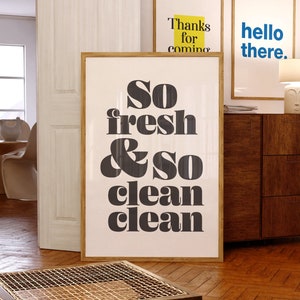 May include: Black and white typography print with the text "So fresh & so clean clean" in a modern, bold font style. The print is framed in a light wood frame and is hanging on a wall.