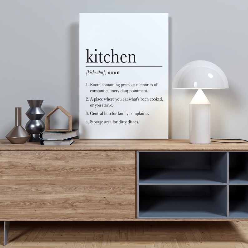 May include: A white canvas print with a black and white definition of the word "kitchen" with four bullet points describing the room. The print is hanging on a wall above a wooden cabinet with a blue shelf unit.
