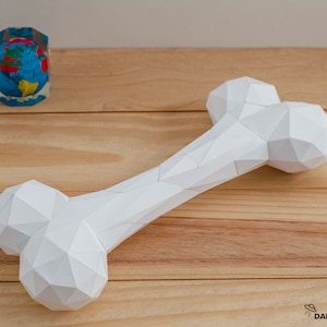 Könnte beinhalten: Ein weißer Papierknochen in Form eines Kauspielzeugs für Hunde. Der Knochen besteht aus gefaltetem Papier und hat ein geometrisches Design.