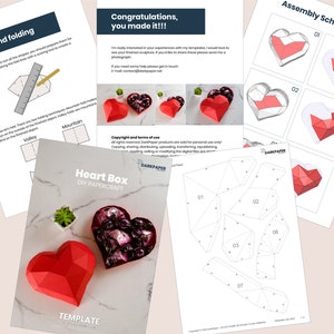 May include: A printable papercraft template for a heart-shaped box. The template includes instructions for scoring and folding the paper to create a 3D box. The image also shows a completed heart box with a red and white color scheme.