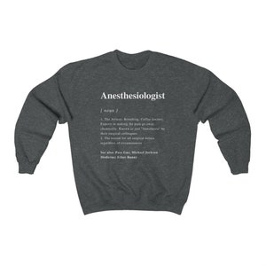 May include: A dark grey sweatshirt with a white print that defines the word "Anesthesiologist" as a noun. The definition includes the phrase "Experts in making the pain go away...chemically." and "Known as just "Anesthesia" by their surgical colleagues."