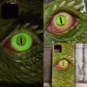 May include: A green and brown phone case with a large, glowing green eye graphic. The eye is surrounded by textured skin and teeth.