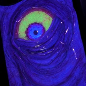 May include: A phone case with a glowing, blue eye and a green iris. The eye is surrounded by a swirling, purple and blue background.
