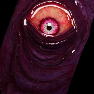 May include: A close-up of a purple phone case with a large, fleshy, pink eye with a black pupil. The eye is surrounded by a fleshy, purple, textured surface.