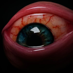May include: Close-up of a glass eye with a red, veiny sclera and a blue iris. The pupil is black and the eye is glossy.