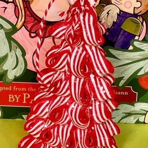 May include: A conical ornament shaped like a Christmas tree, constructed from numerous red and white striped candy cane loops. The structure is topped with a round peppermint candy and features a red and white twisted string for hanging purposes.
