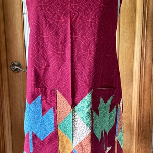 May include: A burgundy apron with a geometric pattern and a patchwork pocket featuring colorful leaf designs.