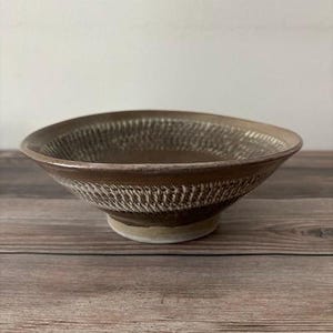 May include: A brown ceramic bowl with a white and brown patterned design. The bowl has a wide rim and a slightly flared base.