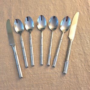 May include: A set of seven pieces of stainless steel flatware consisting of two knives and five spoons. Each piece features a handle designed to resemble bamboo stalks with segmented detailing and a polished, reflective silver finish.