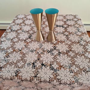May include: Two tall, conical jiggers made of brushed gold-toned metal. Each jigger features a smooth, metallic exterior and a vibrant, solid turquoise interior lining. The two identical bar tools are positioned upright, side by side.