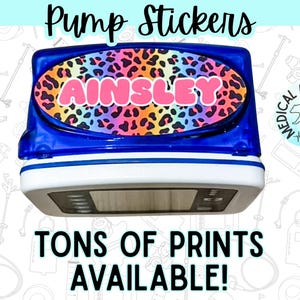 May include: A blue and white insulin pump decorated with a colourful rainbow leopard print sticker featuring the name AINSLEY in pink letters. The image includes the text Pump Stickers and TONS OF PRINTS AVAILABLE along with a bear logo.