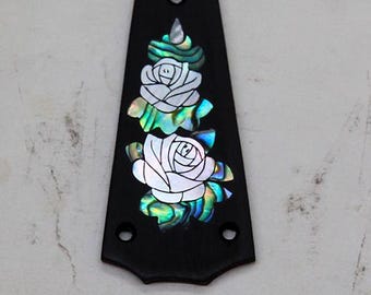 May include: A black guitar truss rod cover featuring an inlaid mother-of-pearl design of two roses with iridescent green and blue abalone shell leaves. The tapered, triangular plate includes three pre-drilled screw holes for attachment.