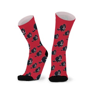 May include: A pair of red socks with a black Tasmanian devil pattern. The socks are made of a soft, comfortable material and have a black toe and heel.