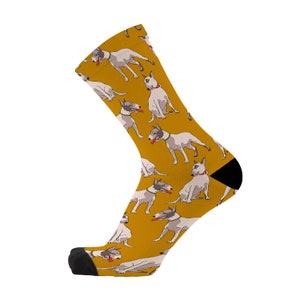 Peut inclure: Une paire de chaussettes jaunes avec un motif de chien bull terrier blanc. Les chaussettes sont noires au niveau des orteils et du talon.