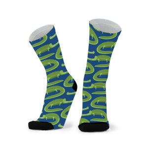 May include: A pair of blue socks with a repeating pattern of green alligators. The socks have black toes and heels.
