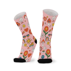 Könnte beinhalten: Ein Paar rosa Socken mit einem sich wiederholenden Muster von Retro-Illustrationen. Das Design umfasst Blumen, Pilze, Herzen, Regenbogen und Friedenszeichen. Die Socken haben schwarze Fersen und Zehen und weiße Oberteile.