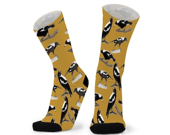 May include: Mustard yellow socks featuring a repeating pattern of black and white magpies. The socks have black heels and toes, and white tops. The magpies are perched on branches.