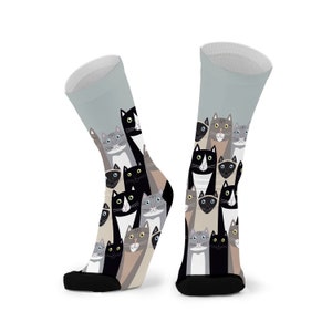 May include: A pair of grey socks with a colourful pattern of cats. The cats are in various poses and colours, including black, white, grey, and brown.
